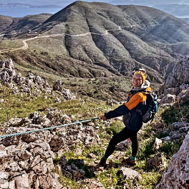 Wanderin gesichert an einer Felskante über grünen Hügeln