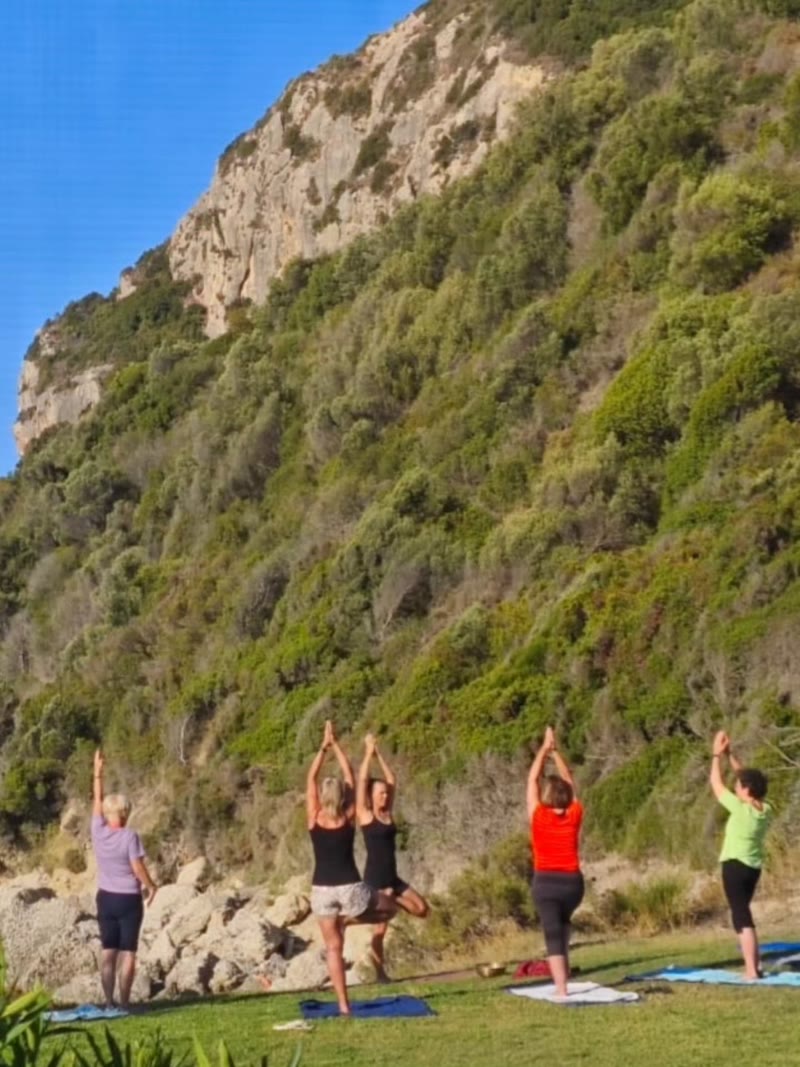 Gruppe beim Yoga an einem Hang über dem Meer
