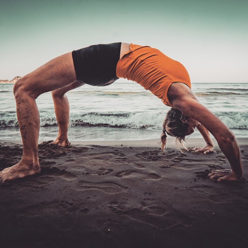 Yoga-Brücke auf dunklem Sand am Meer